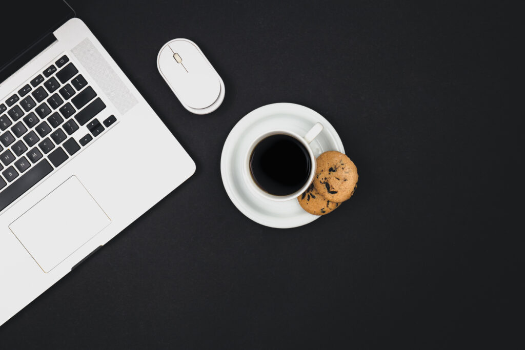 laptop, computer mouse, a cup of coffee and cookies on a black background.